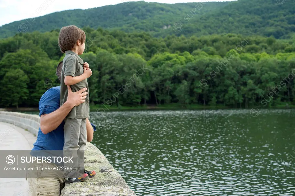 Father holding son standing on stone wall