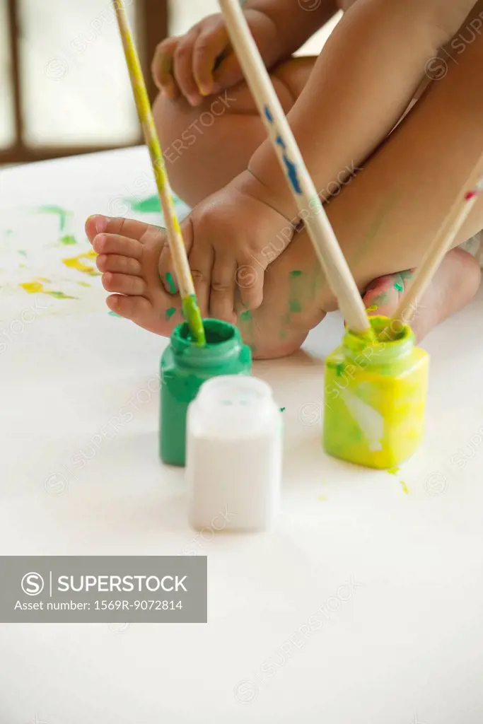 Baby sitting with paints and paintbrushes, cropped