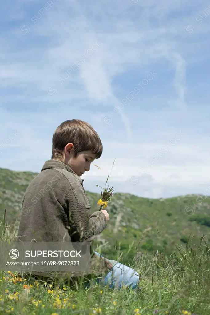 Boy kneeling on meadow with flowers in hand