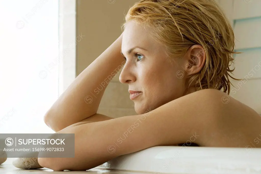 Mid_adult woman relaxing in bath, contemplatively looking away, portrait