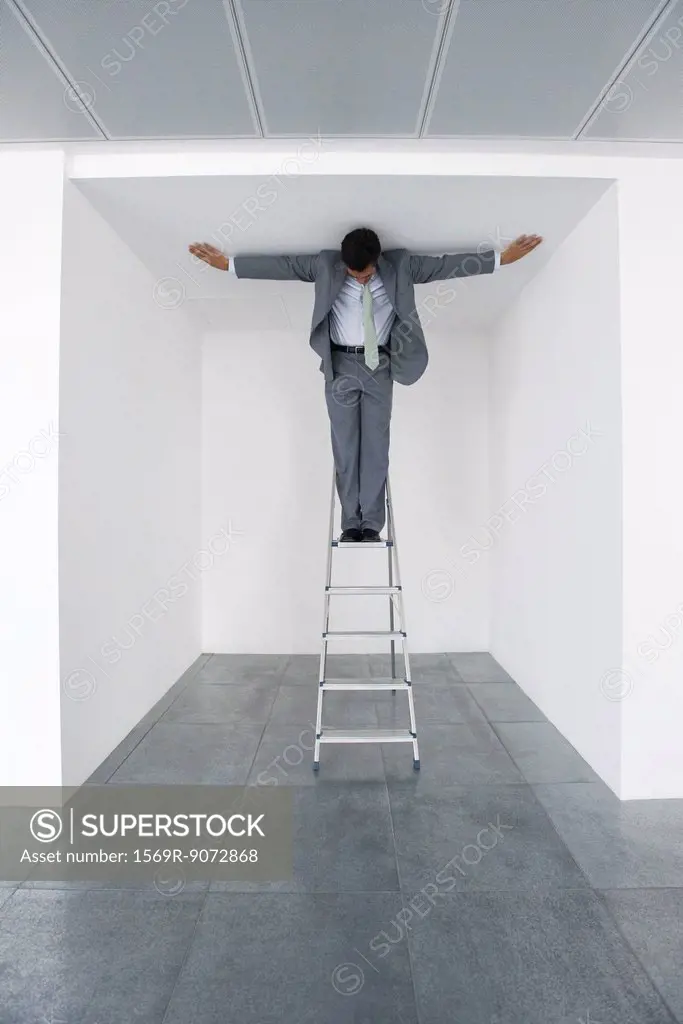 Executive standing on stepladder, arms outstretched on ceiling