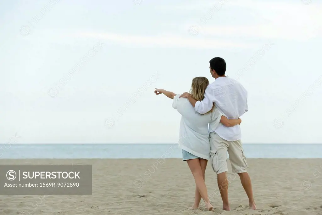 Couple walking together at the beach, woman pointing at sea
