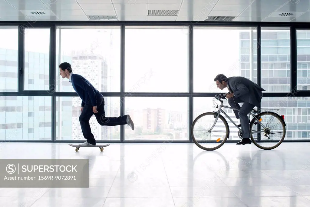 One businessman skateboarding, the other riding bicycle
