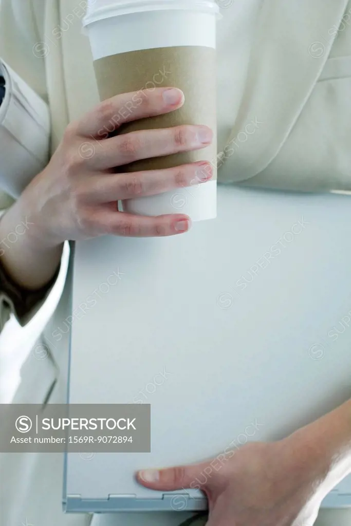 Woman holding disposable coffee cup, mid section