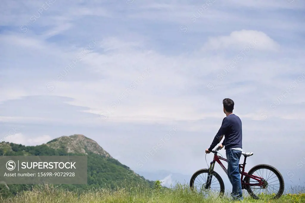 Man standing by mountain bike, enjoying scenic mountain view, rear view