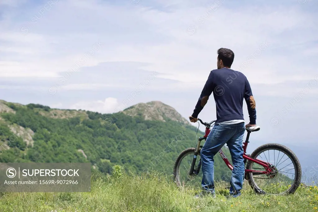 Man standing by mountain bike, enjoying scenic mountain view, rear view