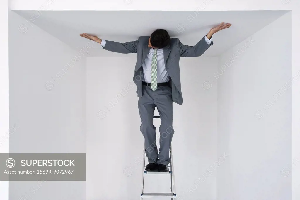 Executive standing on stepladder, arms outstretched on ceiling