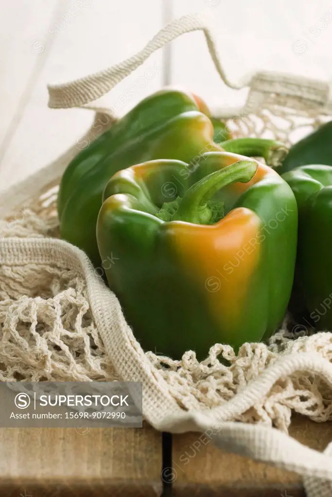 Fresh green bell peppers in mesh shopping bag