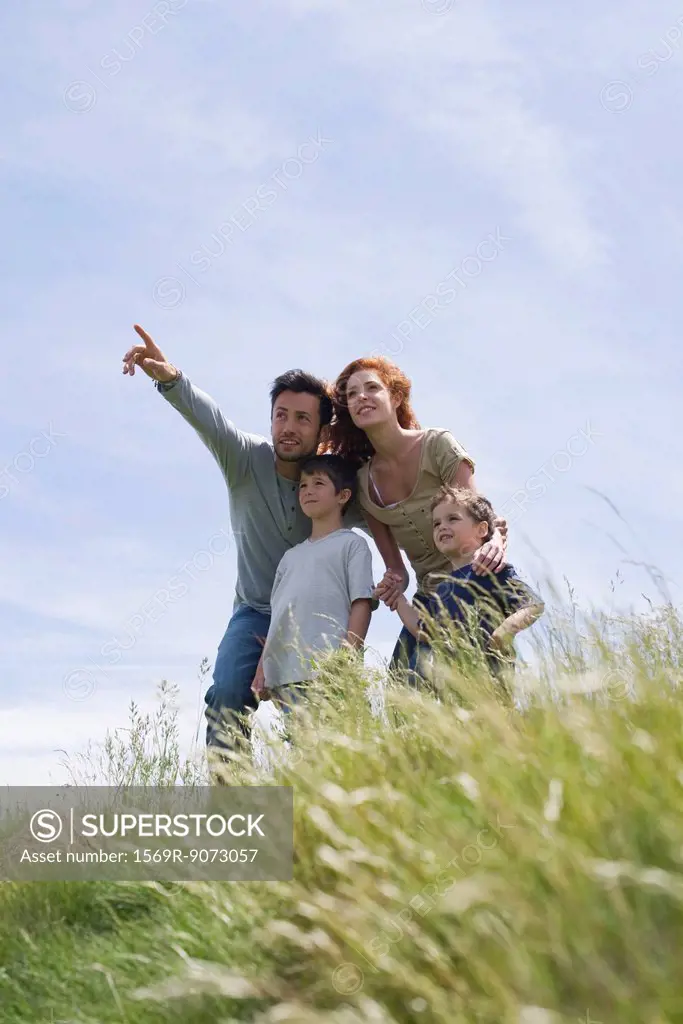 Parents and two boys standing on meadow, father pointing into distance