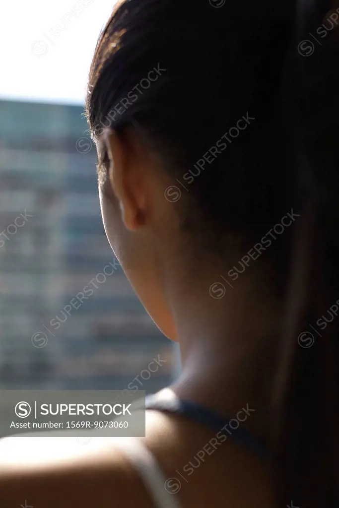 Woman by window, rear view, backlit