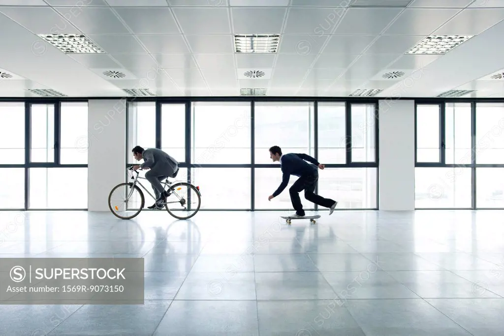 One businessman riding bicycle, the other skateboarding