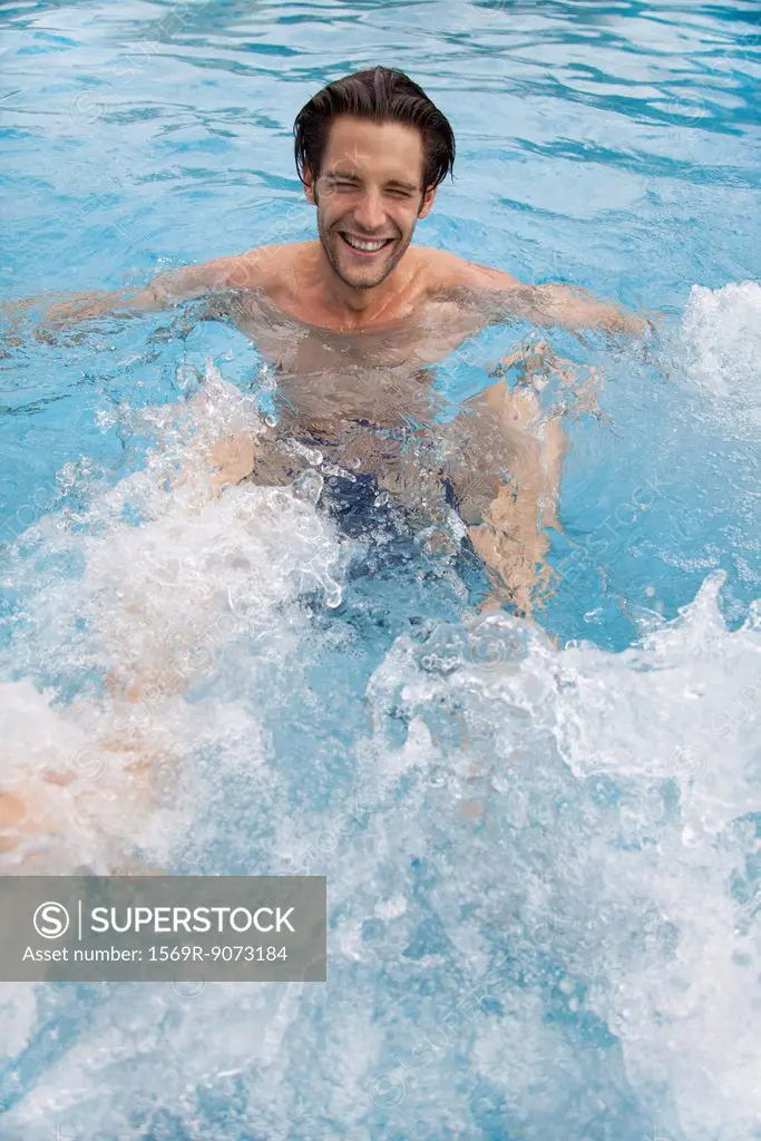 Young man kicking water in swimming pool