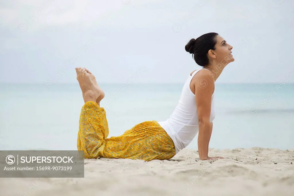 Mature woman practicing yoga on beach, side view