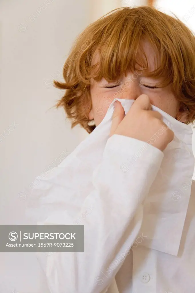 Boy blowing nose on tissue with eyes closed