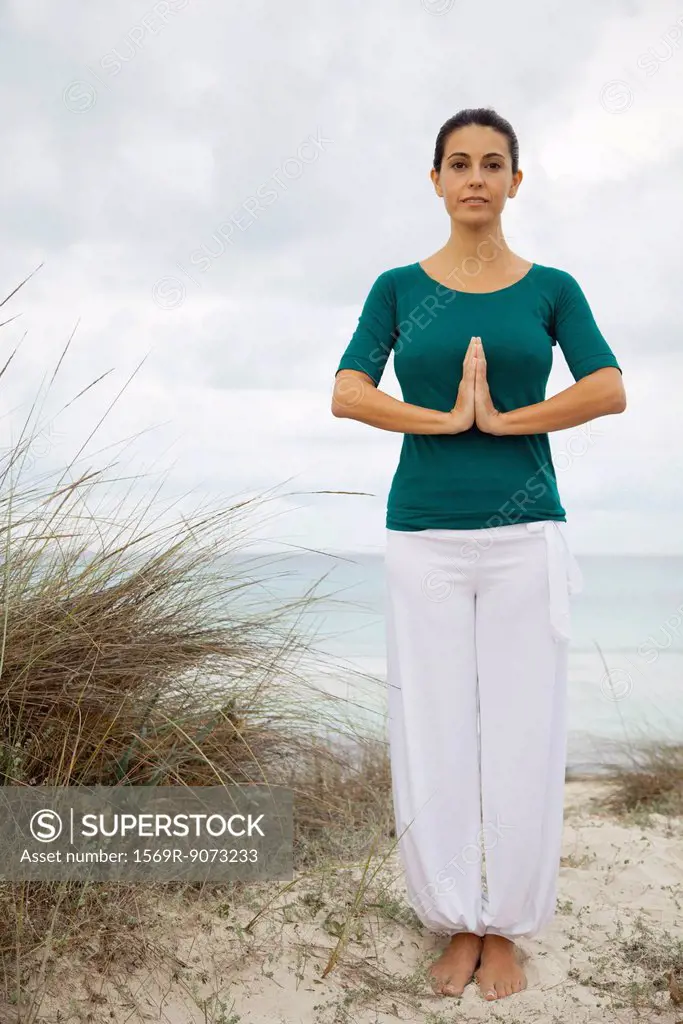Mature woman in yoga prayer position on beach, portrait