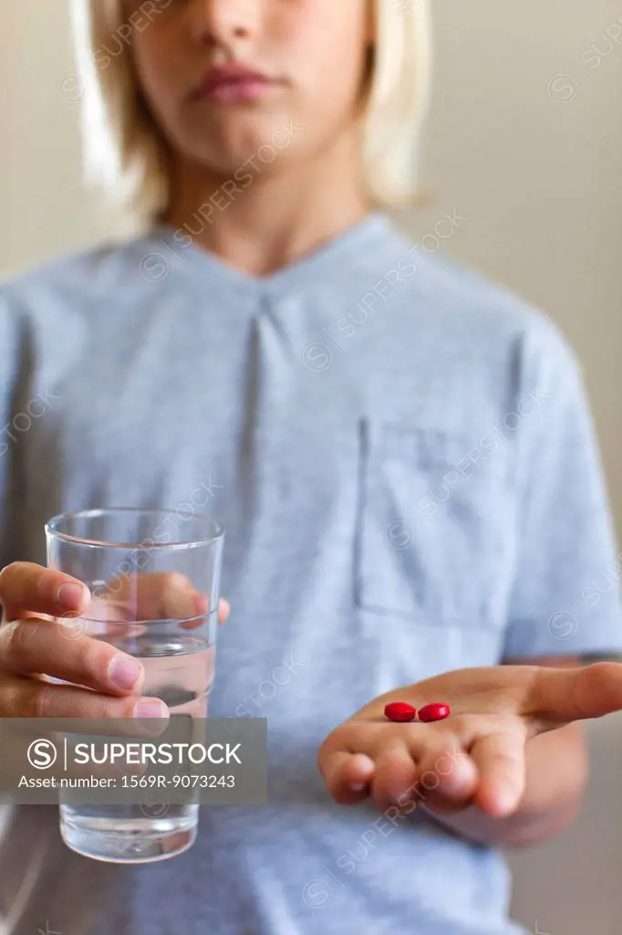 Boy holding glass of water and tablets, mid section