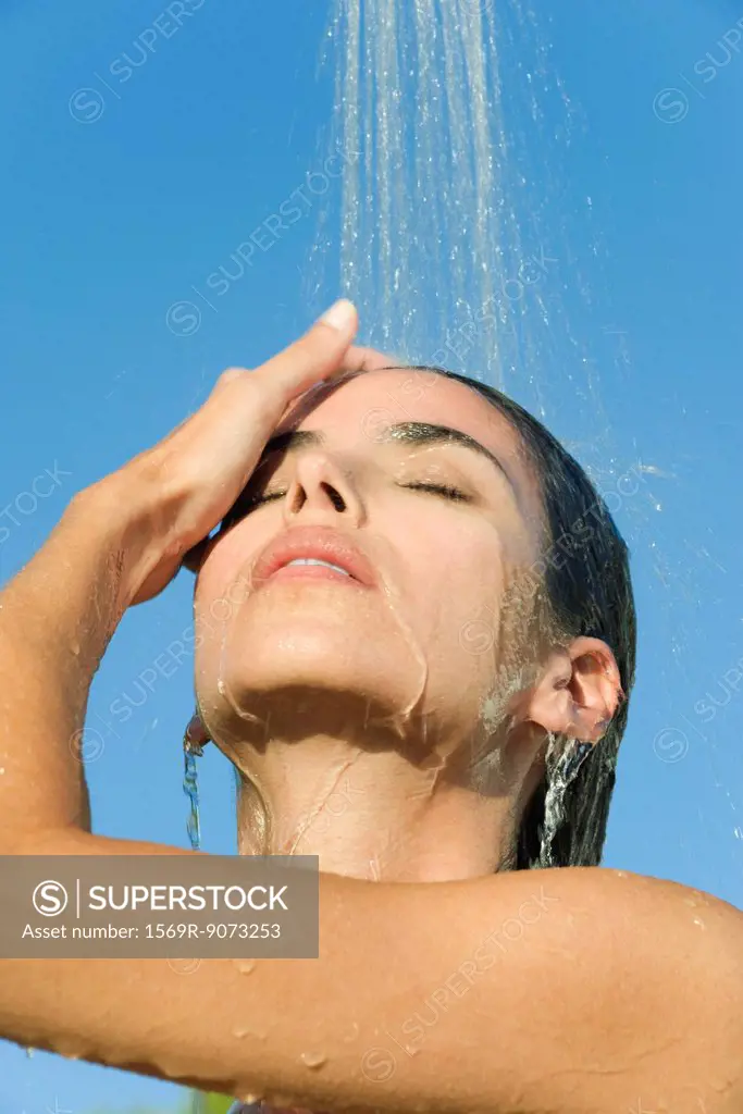 Mid_adult woman under shower outdoors with eyes closed