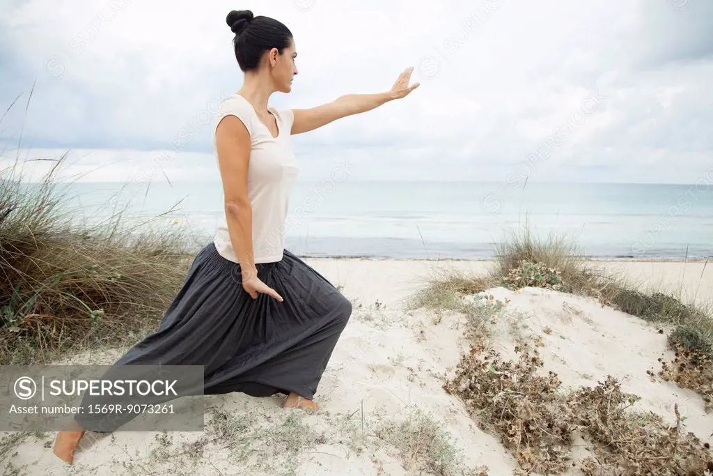 Woman practicing tai chi chuan on beach, side view