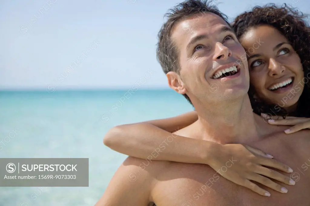 Couple together at the beach, looking up and smiling