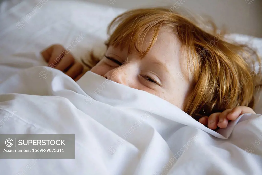 Boy lying in bed with bed sheet covering face