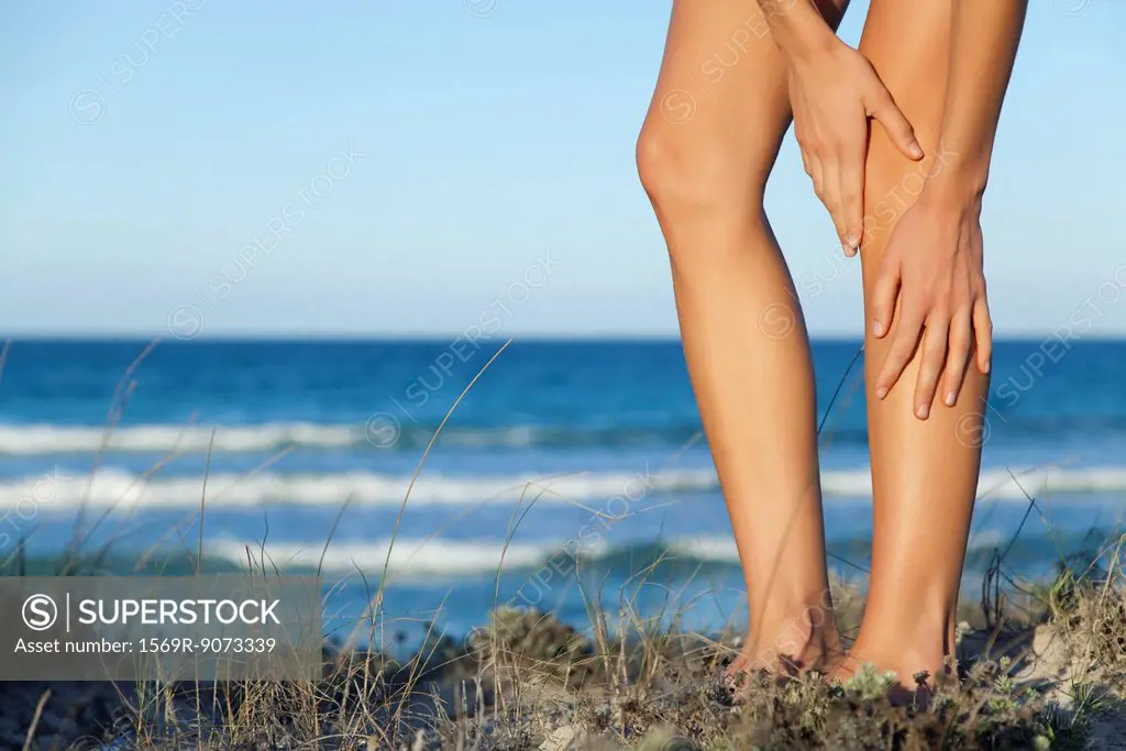 Woman rubbing legs on beach, low section