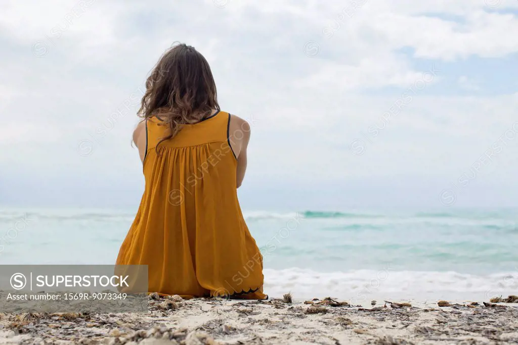 Young woman sitting on beach looking at view, rear view