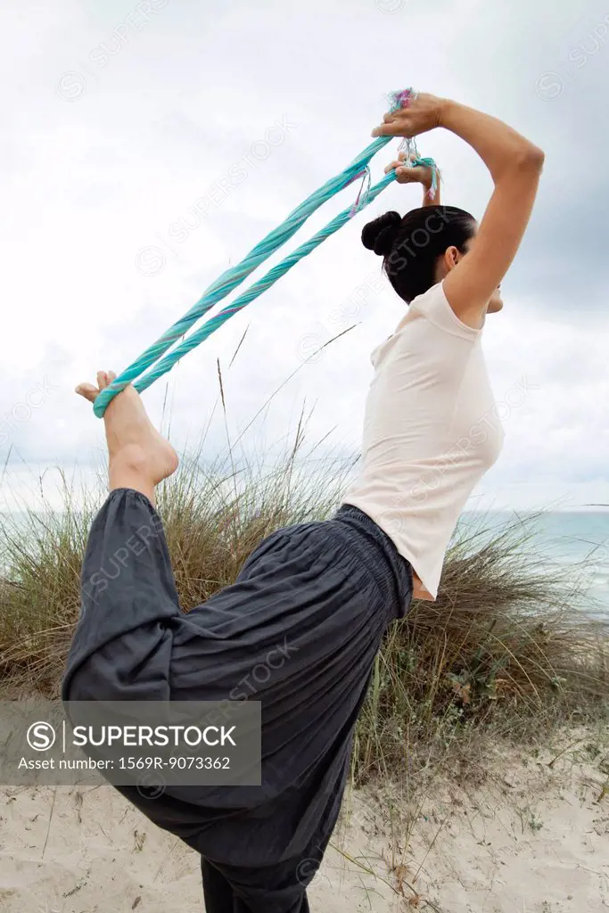 Woman in Natarajasana pose on beach, side view