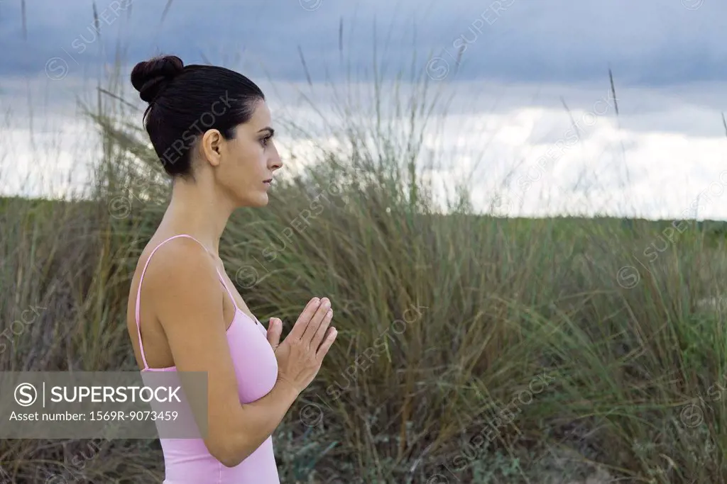 Mature woman in prayer position outdoors, side view