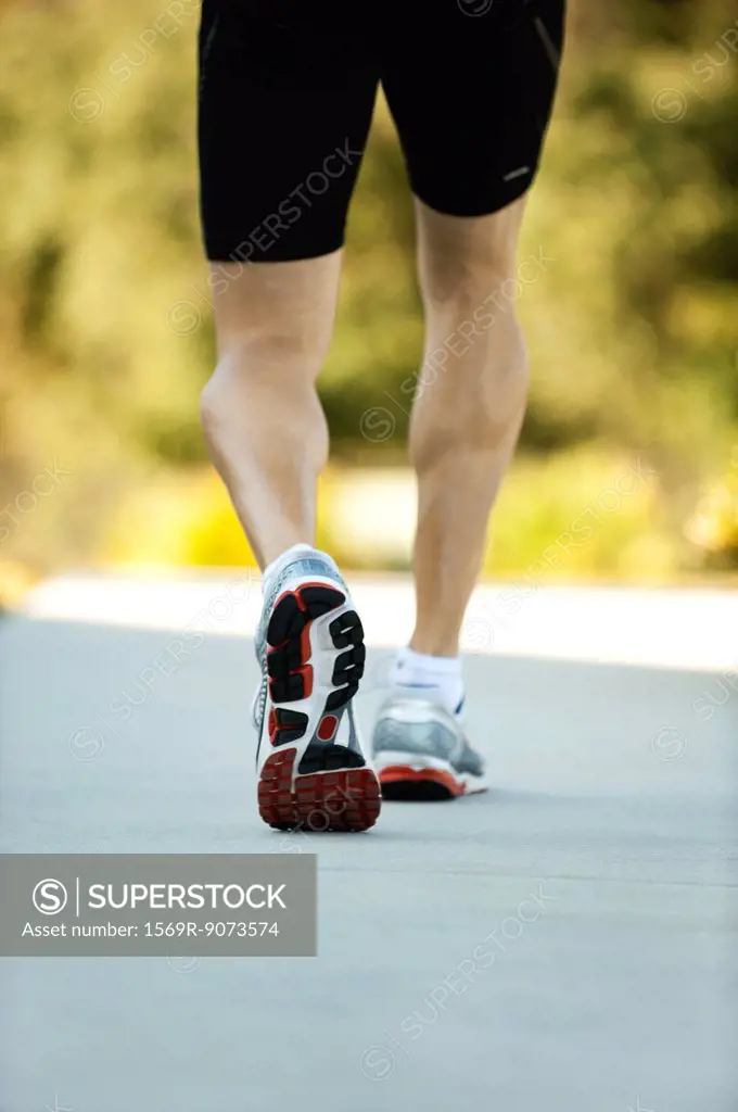 Man in sport shoes walking, low section, rear view
