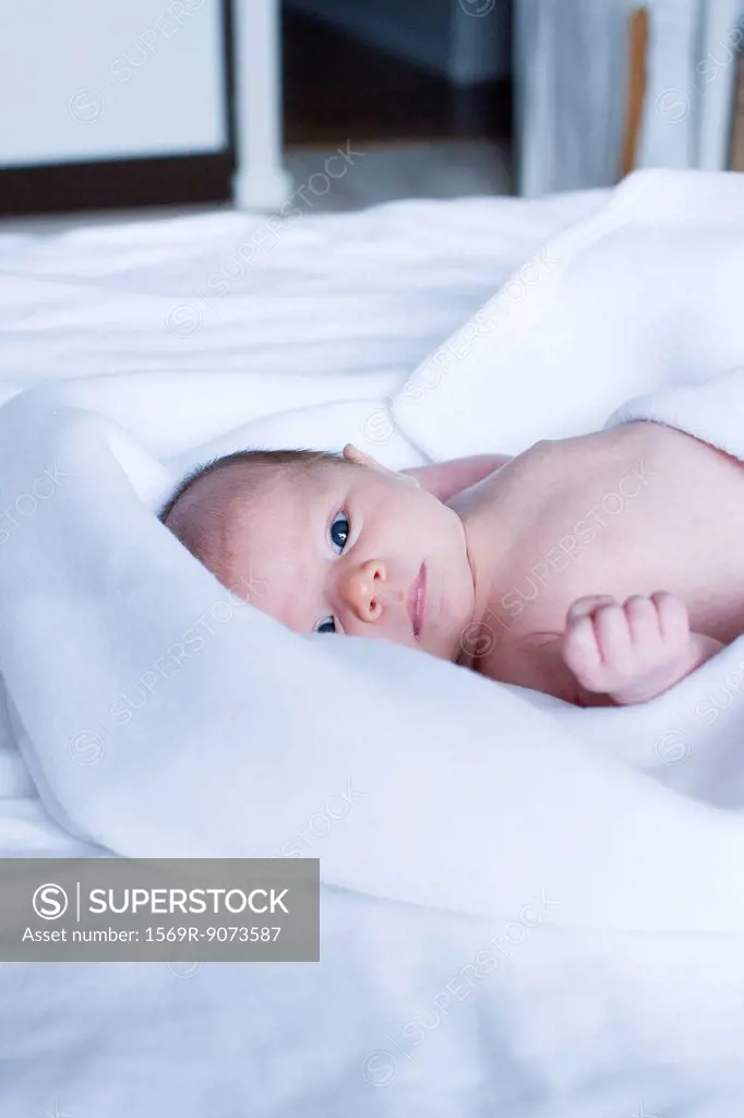Newborn baby lying on bed, looking at camera