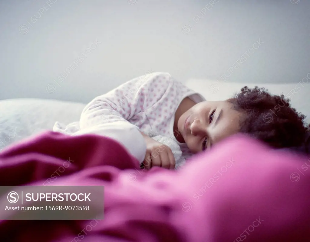 Little girl lying on bed, looking away in thought