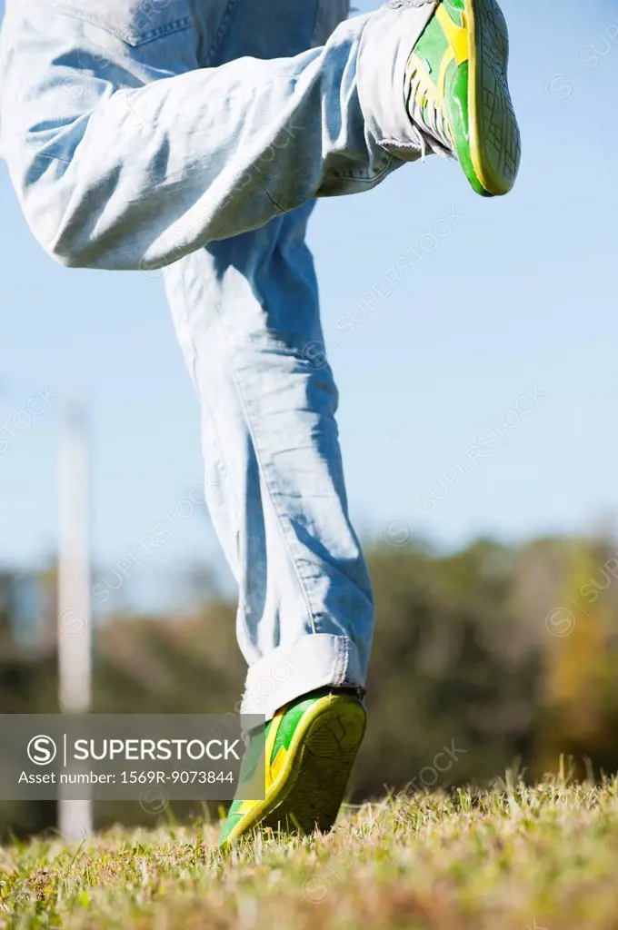 Man in jeans running on grass, low section
