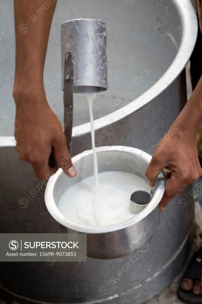 Man ladling fresh milk into pot, cropped