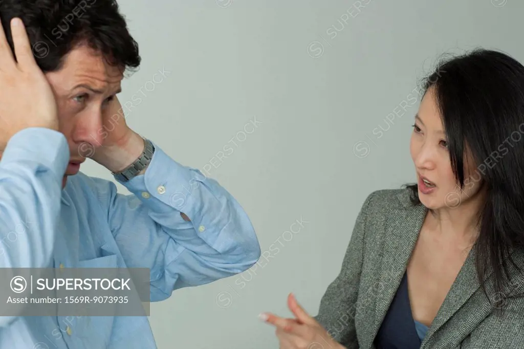 Man and woman arguing, man covering his ears with hands