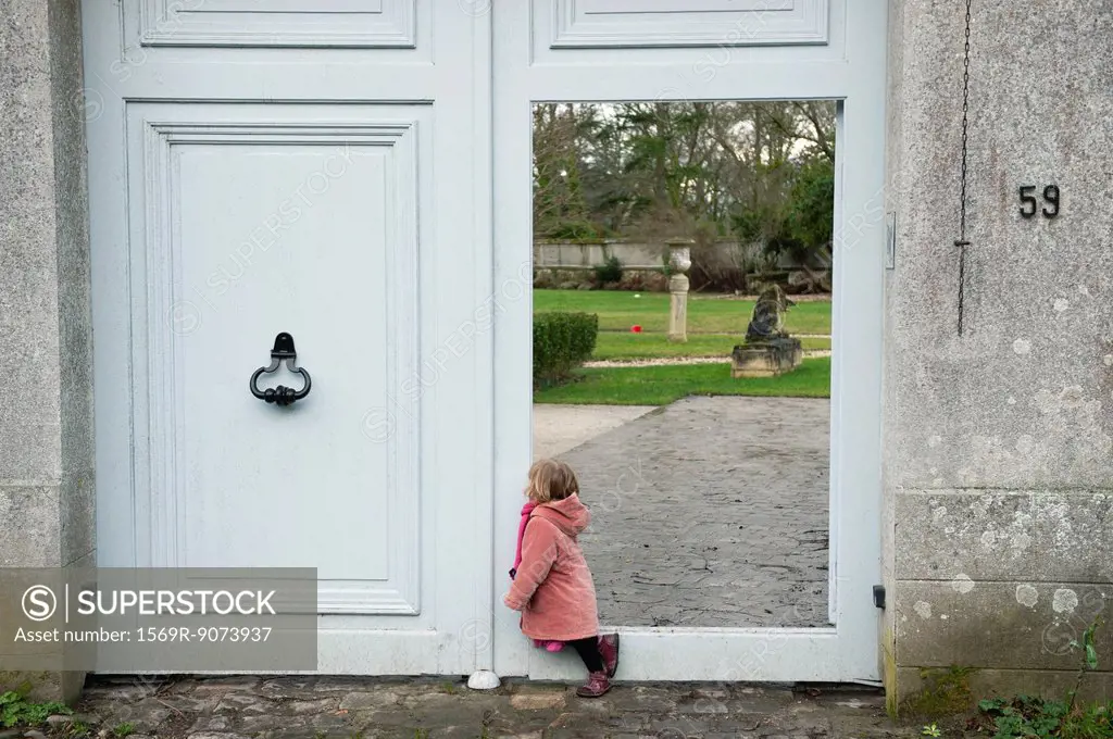 Little girl leaning against open door, looking into courtyard