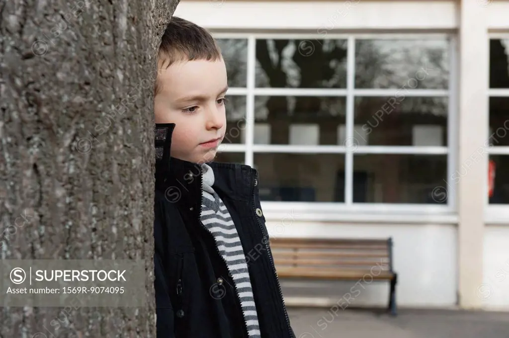 Boy leaning against tree trunk