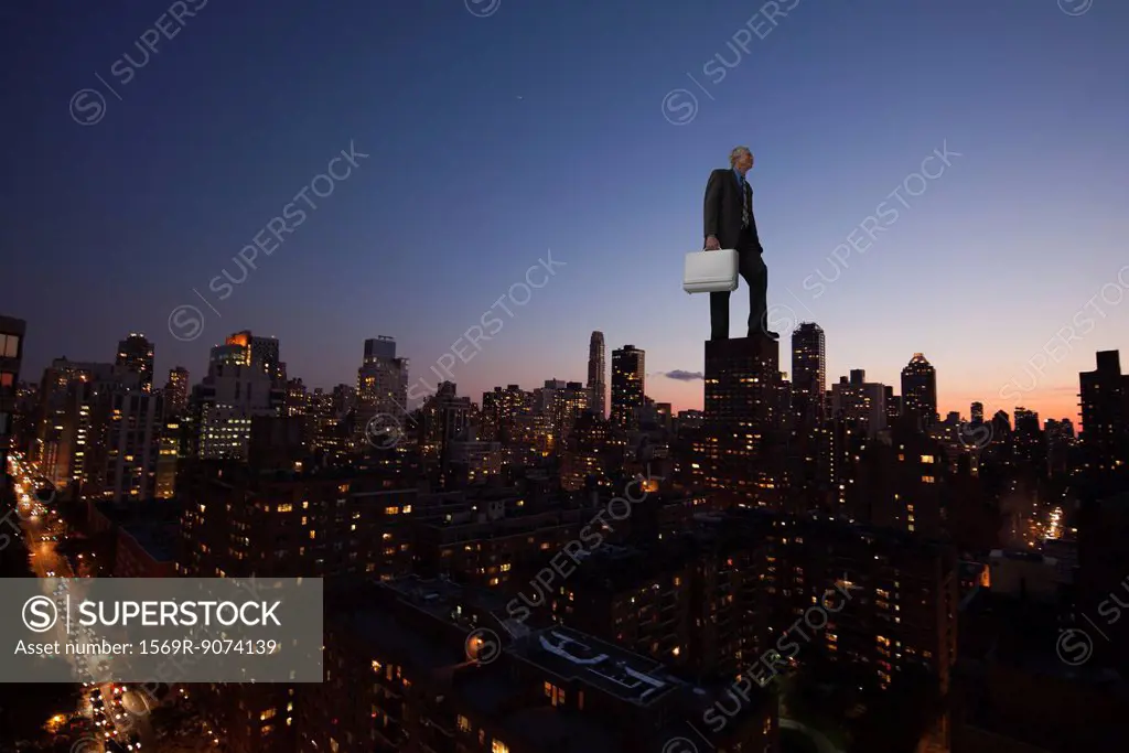 Giant businessman standing on top of skyscraper at dusk