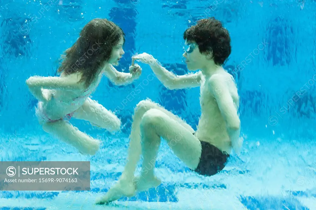 Brother and sister playing underwater in swimming pool