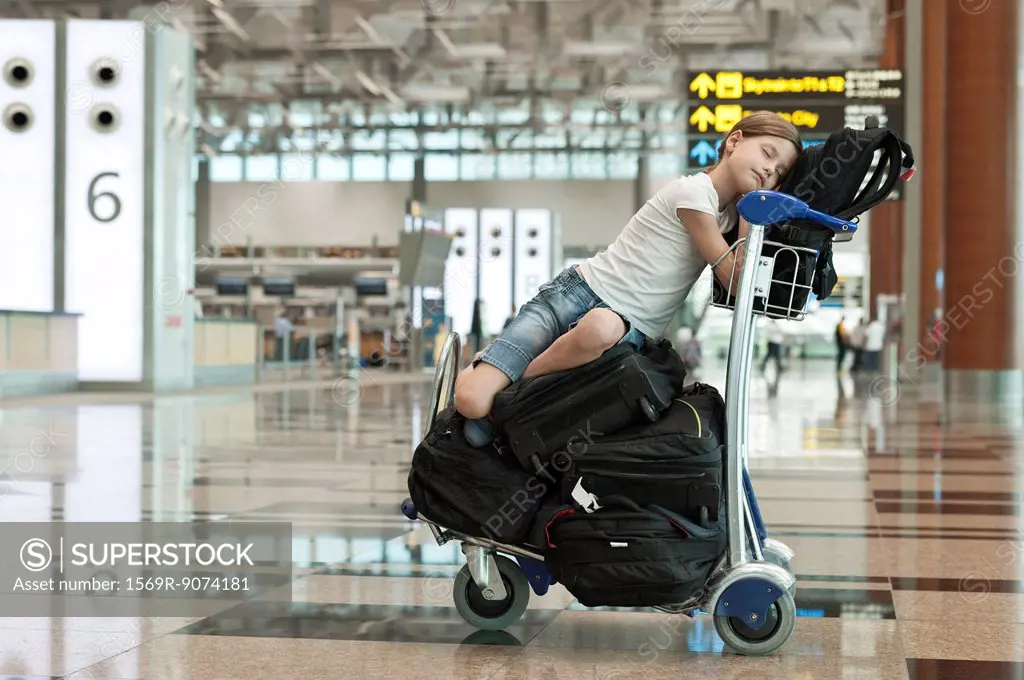 Girl resting on top of luggage cart in airport