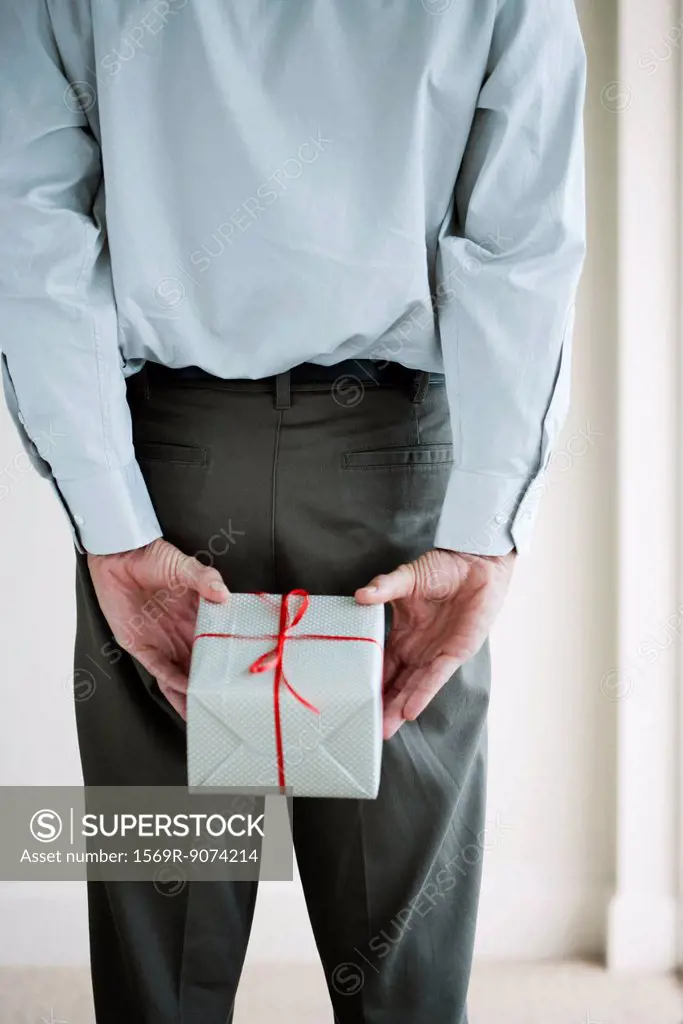 Man holding wrapped gift behind his back, cropped