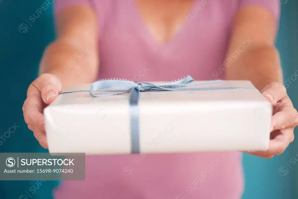 Woman holding out wrapped gift, cropped