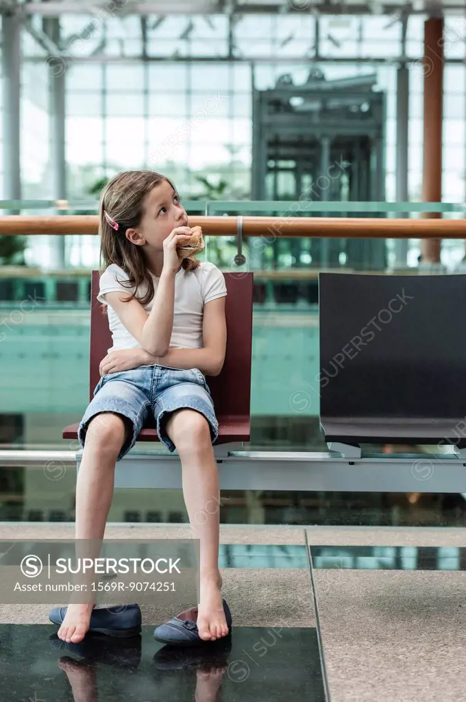 Girl sitting in airport eating sandwich, portrait
