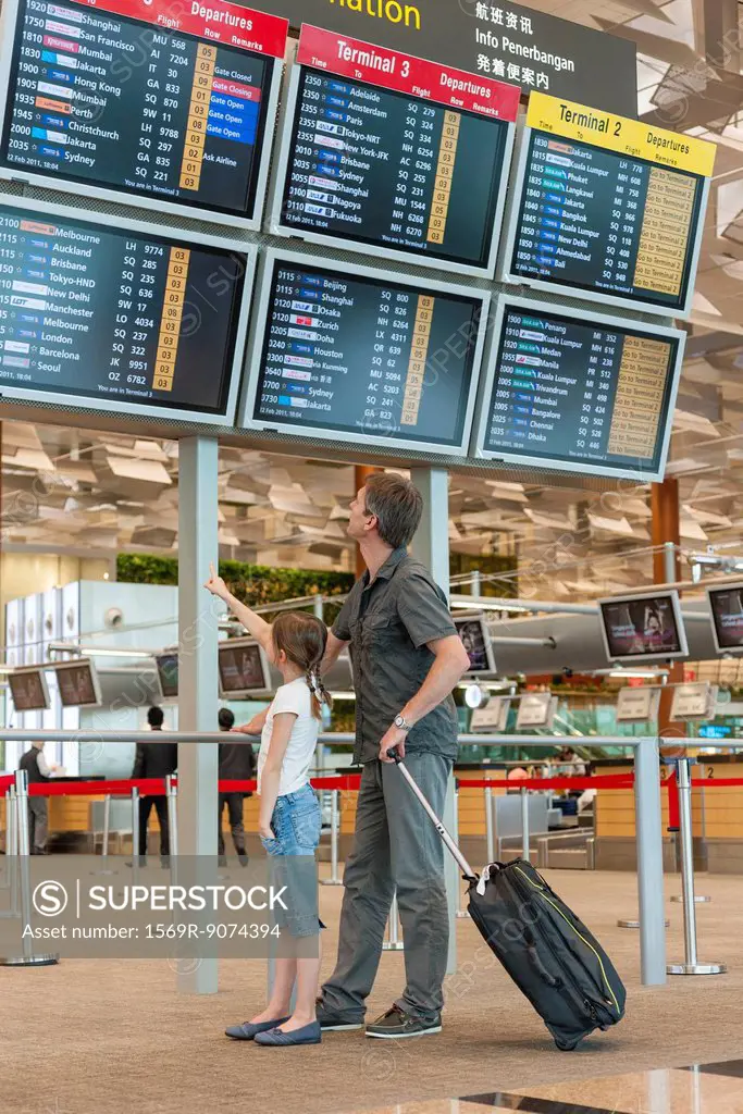 Father and daughter looking at arrival departure board in airport