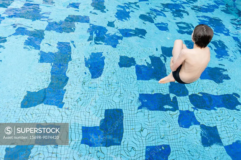 Boy jumping into swimming pool, rear view