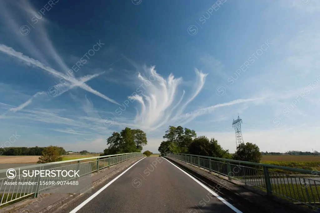 Whispy clouds and vapor trails in sky over bridge