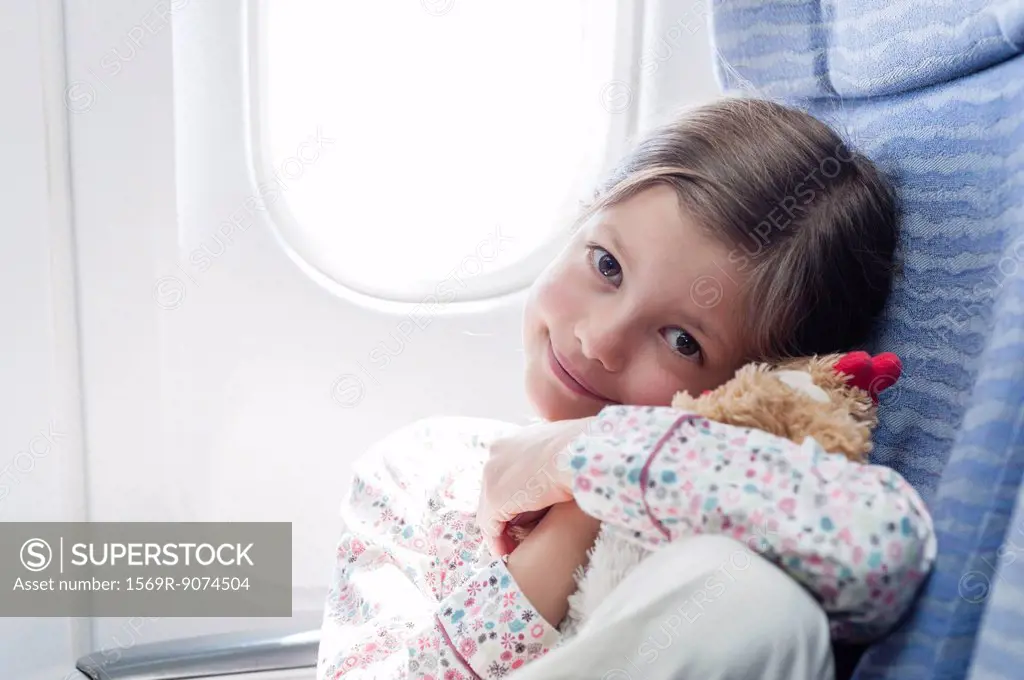Girl holding stuffed toy on airplane, portrait