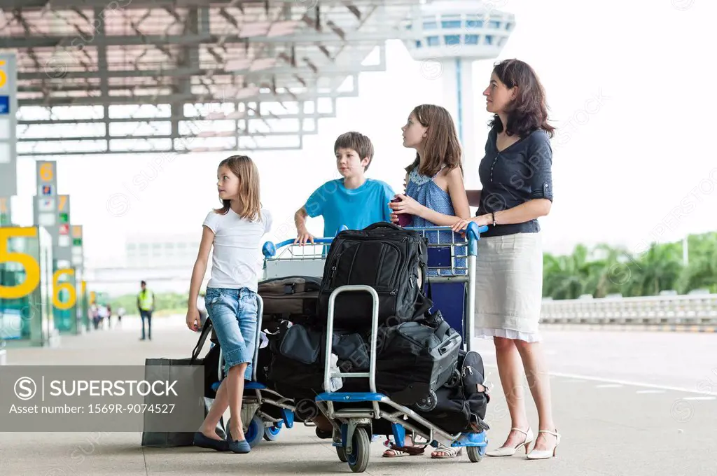Family standing outside of airport with luggage