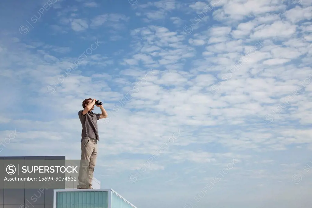 Oversized man standing on rooftop, looking through binoculars