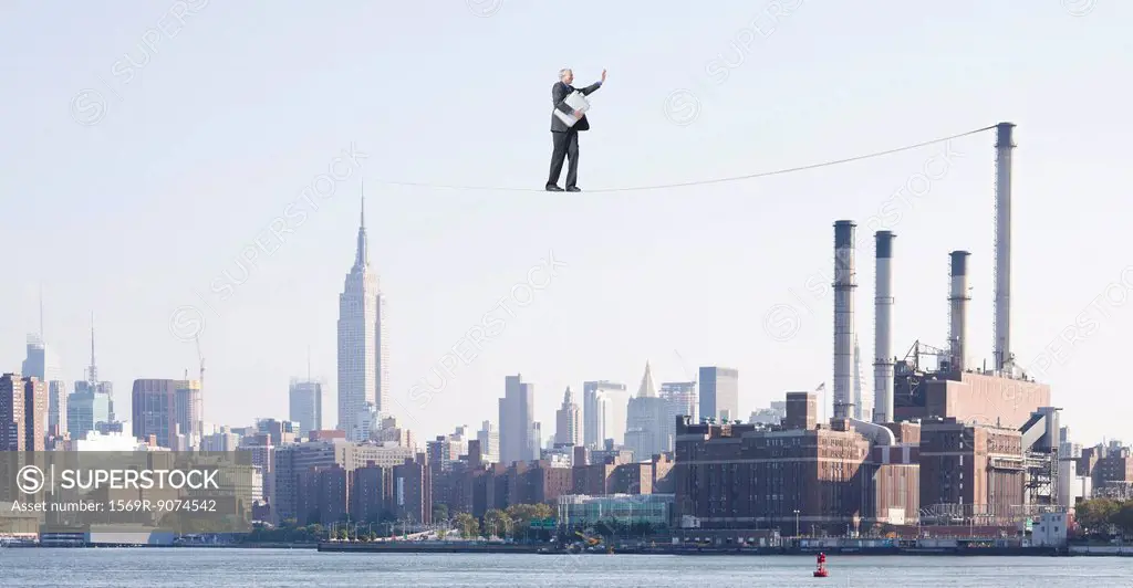Oversized businessman walking on tightrope above city, carrying briefcase stuffed with cash