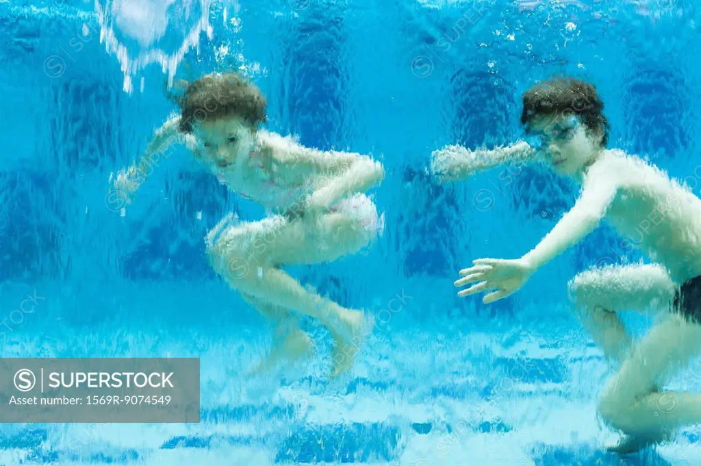 Brother and sister swimming underwater in swimming pool